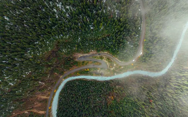 A breathtaking aerial view of lush green forest with a winding road and river cutting through the mountains.