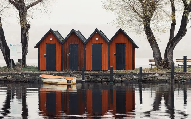 Picturesque red boathouses reflect in a tranquil stream surrounded by autumn trees in Jönköping.