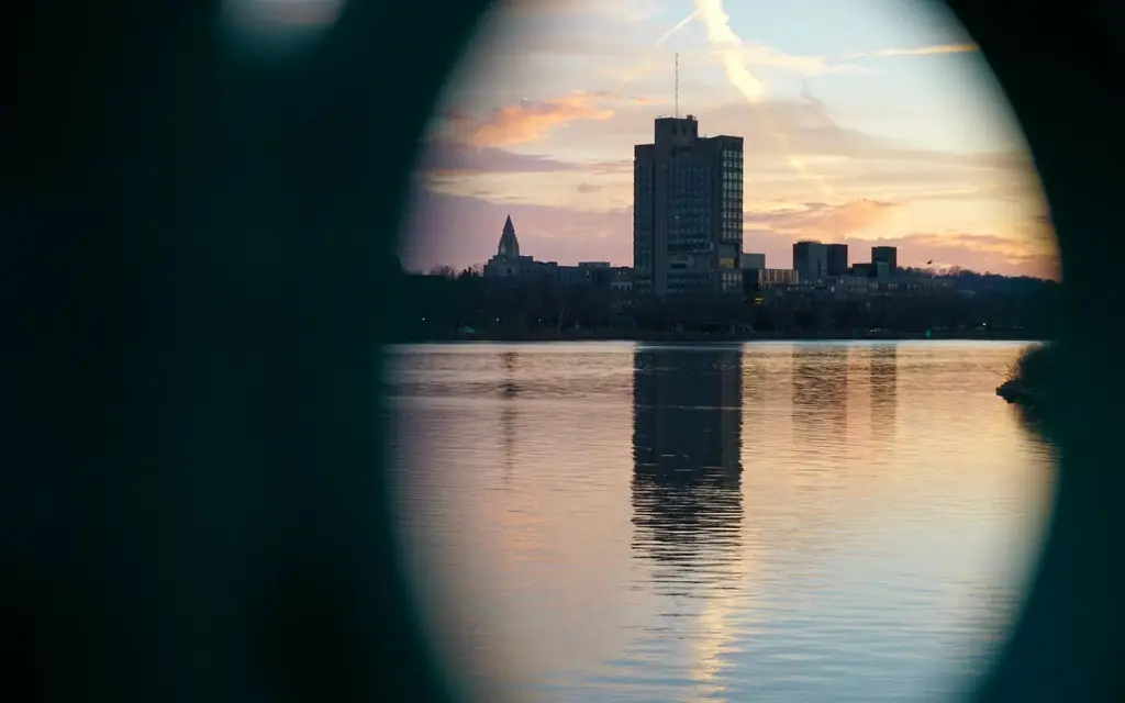 A city skyscraper reflected in a river, captured at sunset through a circular frame.