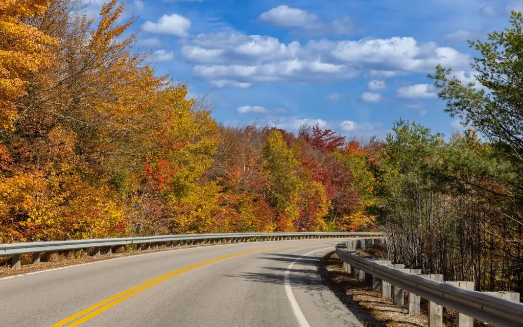 Vibrant fall foliage along a winding road in Franconia, NH, under a clear blue sky.